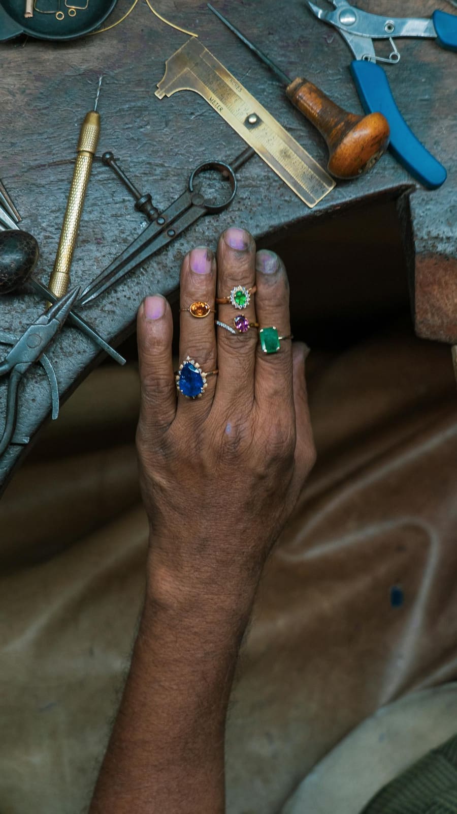 A jeweller's hand wearing sapphire, emerald and citrine rings at a workbench